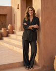 Woman in a black outfit standing against a warm-toned wall with terracotta pots.